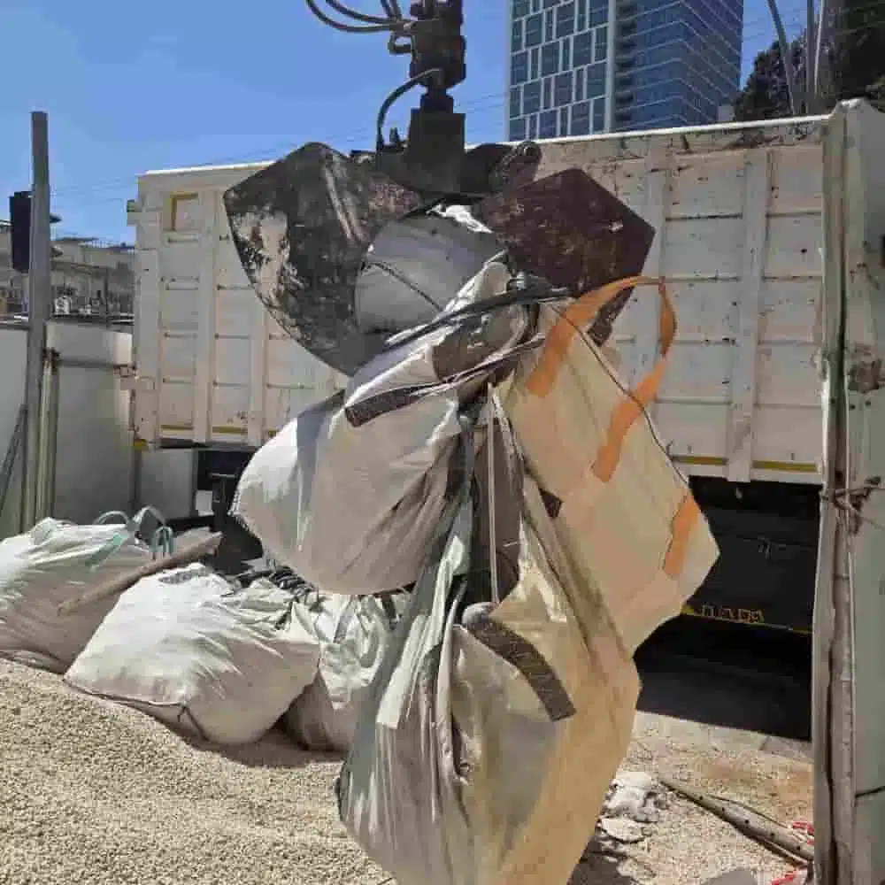 העמסת באלת פסולת בניין למכולה במנוף באתר של אגם